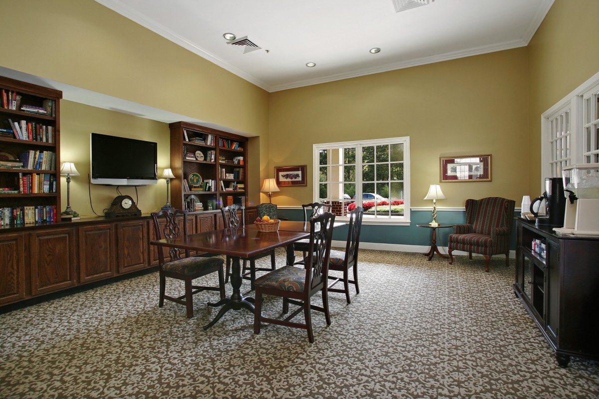 A cozy living room with a table and chairs, bookshelf, television, and lamps.