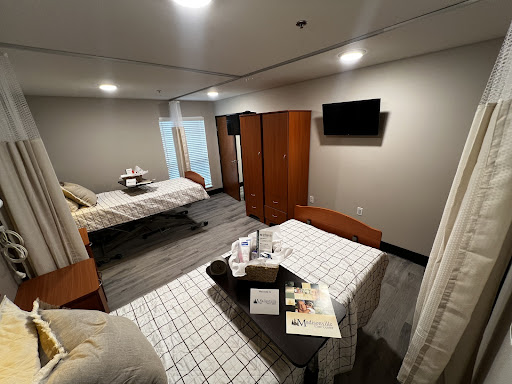 A spacious hospital room equipped with two beds, a wardrobe, and a television.