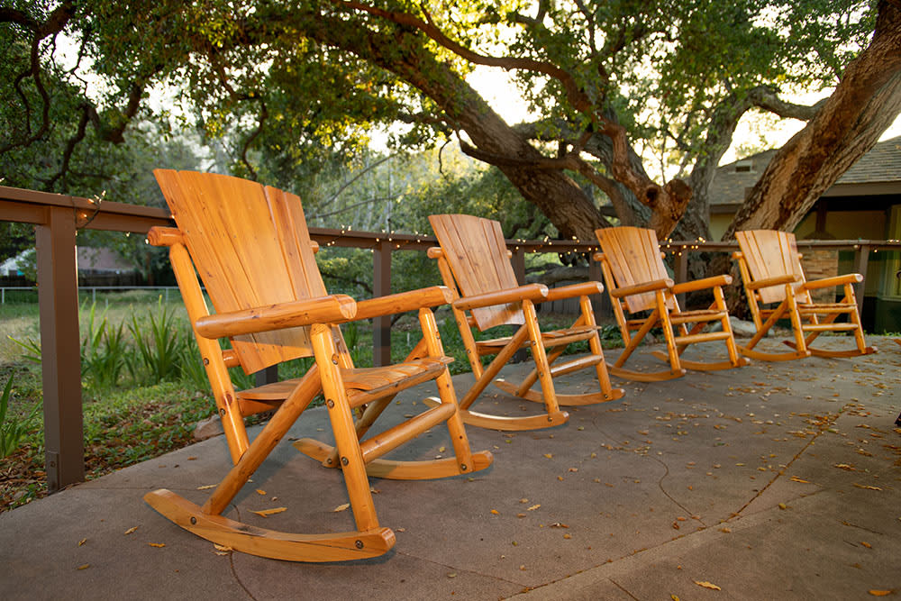 Four wooden rocking chairs on a patio overlooking a garden at sunset.