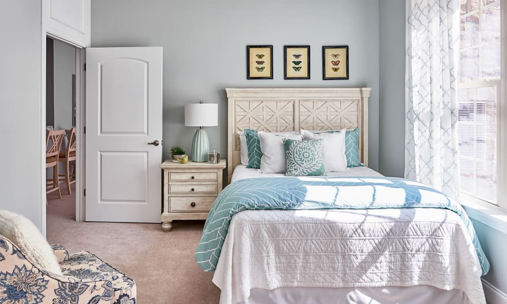 A cozy bedroom with elegant decor, featuring a neatly made bed with blue and white bedding, a nightstand with a lamp, and framed artwork on the wall.