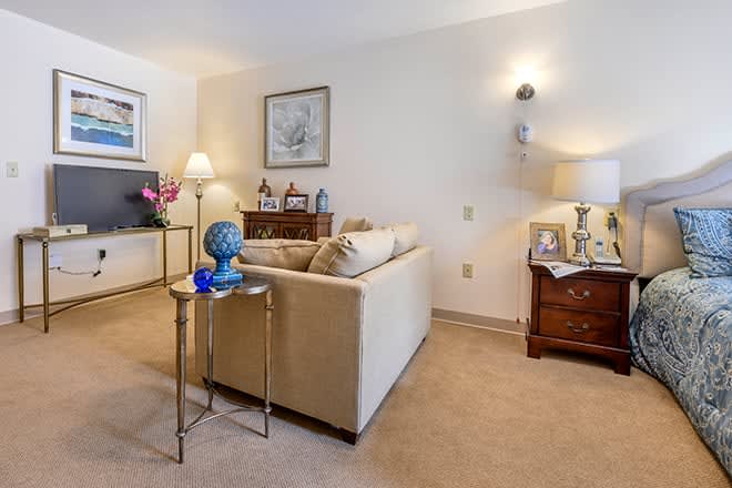 A cozy living room with a beige sofa, decorated with a lamp, side table, and artwork on the walls.