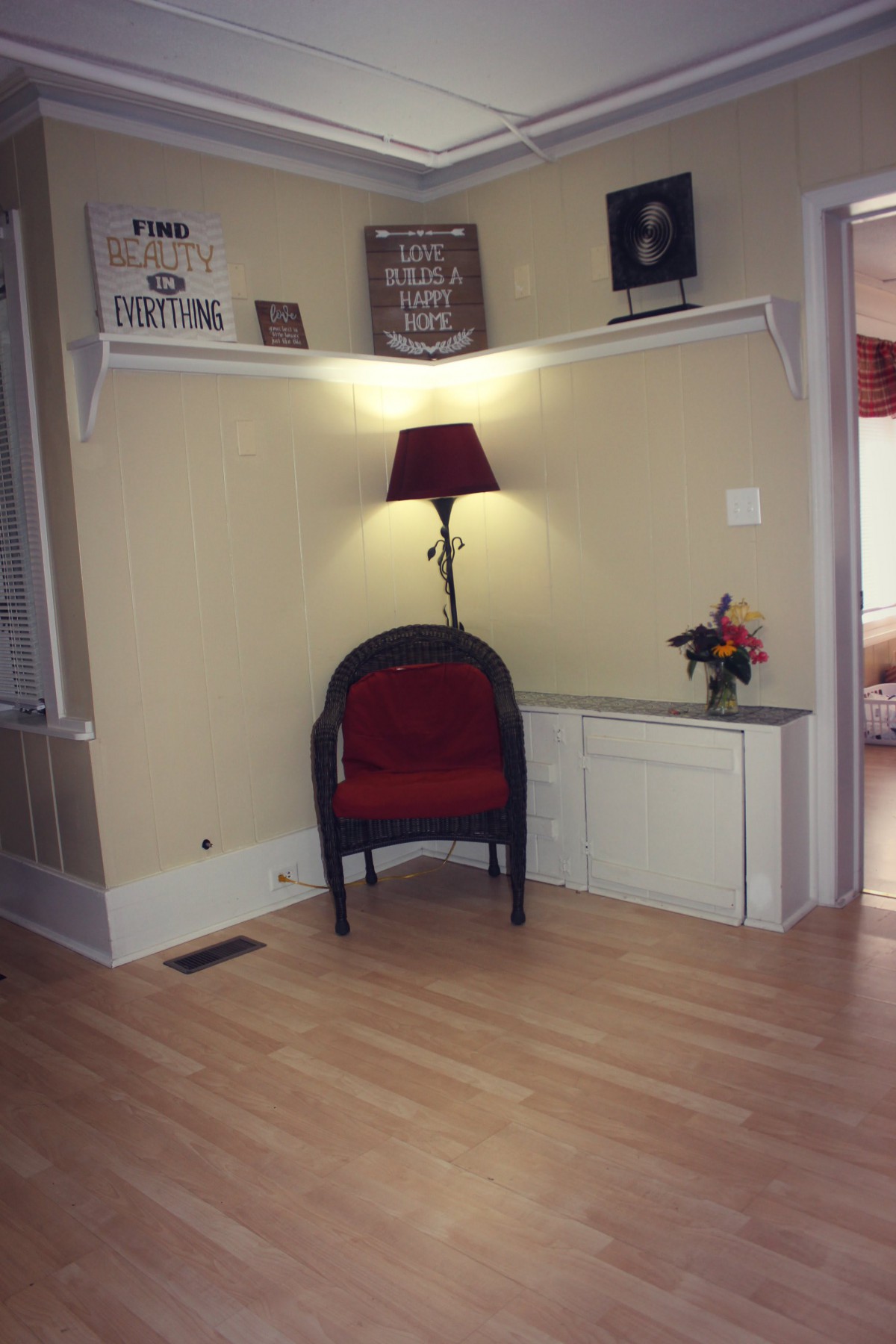 A cozy corner with a red chair, lamp, and decorative shelves.