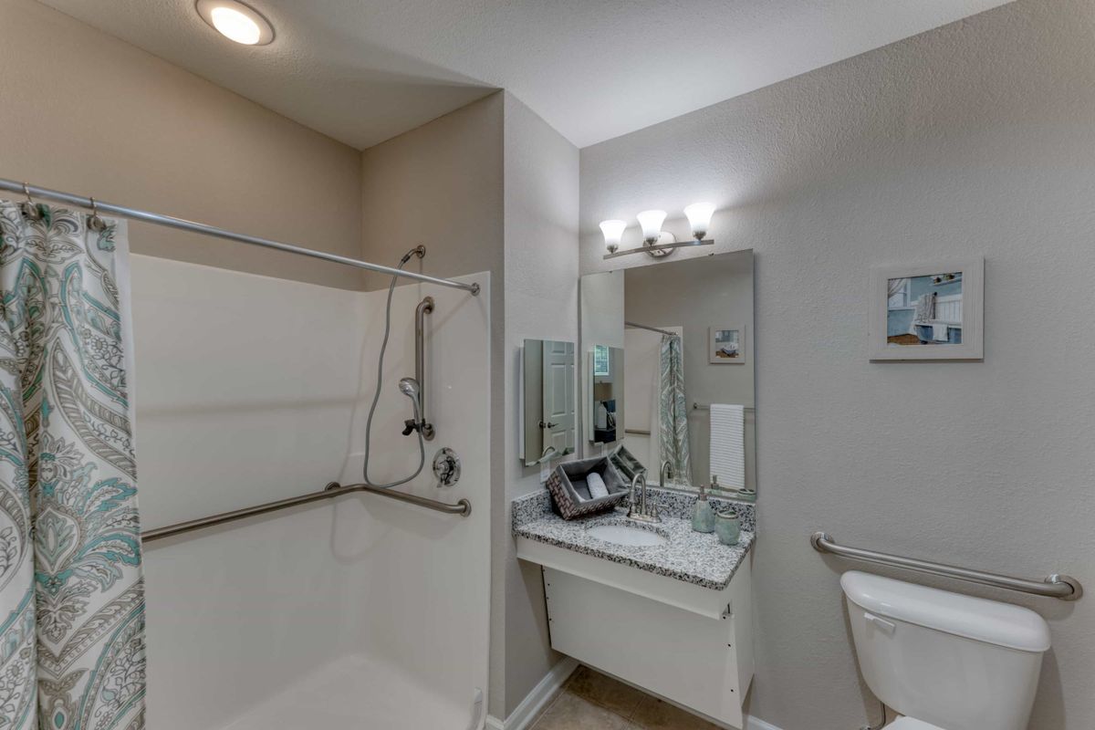 A modern, accessible bathroom with a shower, sink, and mirror.