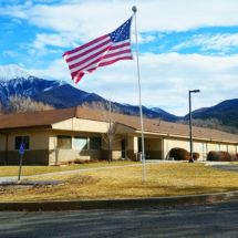 A building with an American flag on a flagpole set against a mountain backdrop.