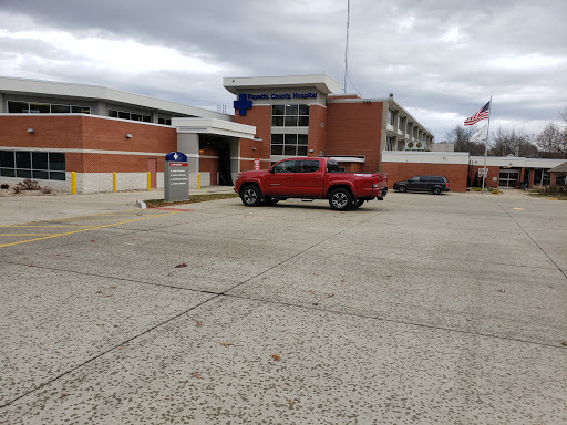 A red vehicle parked outside a modern brick building under a cloudy sky.