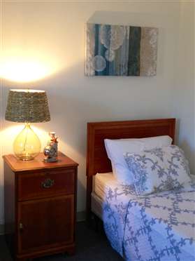 A cozy bedroom corner featuring a nightstand with a lamp and a neatly made bed adorned with patterned bedding.