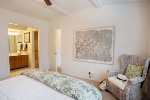 A cozy bedroom with elegant decor, featuring a bed, artwork on the wall, and an inviting chair.