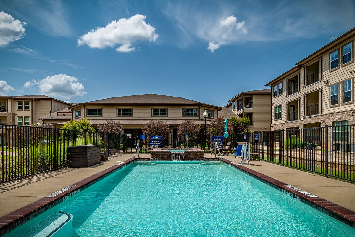 A sunny view of a swimming pool surrounded by apartment buildings under a clear blue sky.