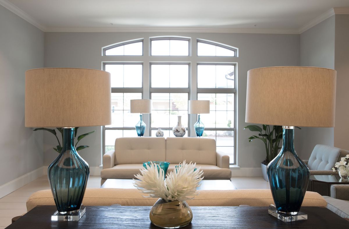 A modern living room with large windows, featuring a beige sofa and two elegant table lamps on either side.