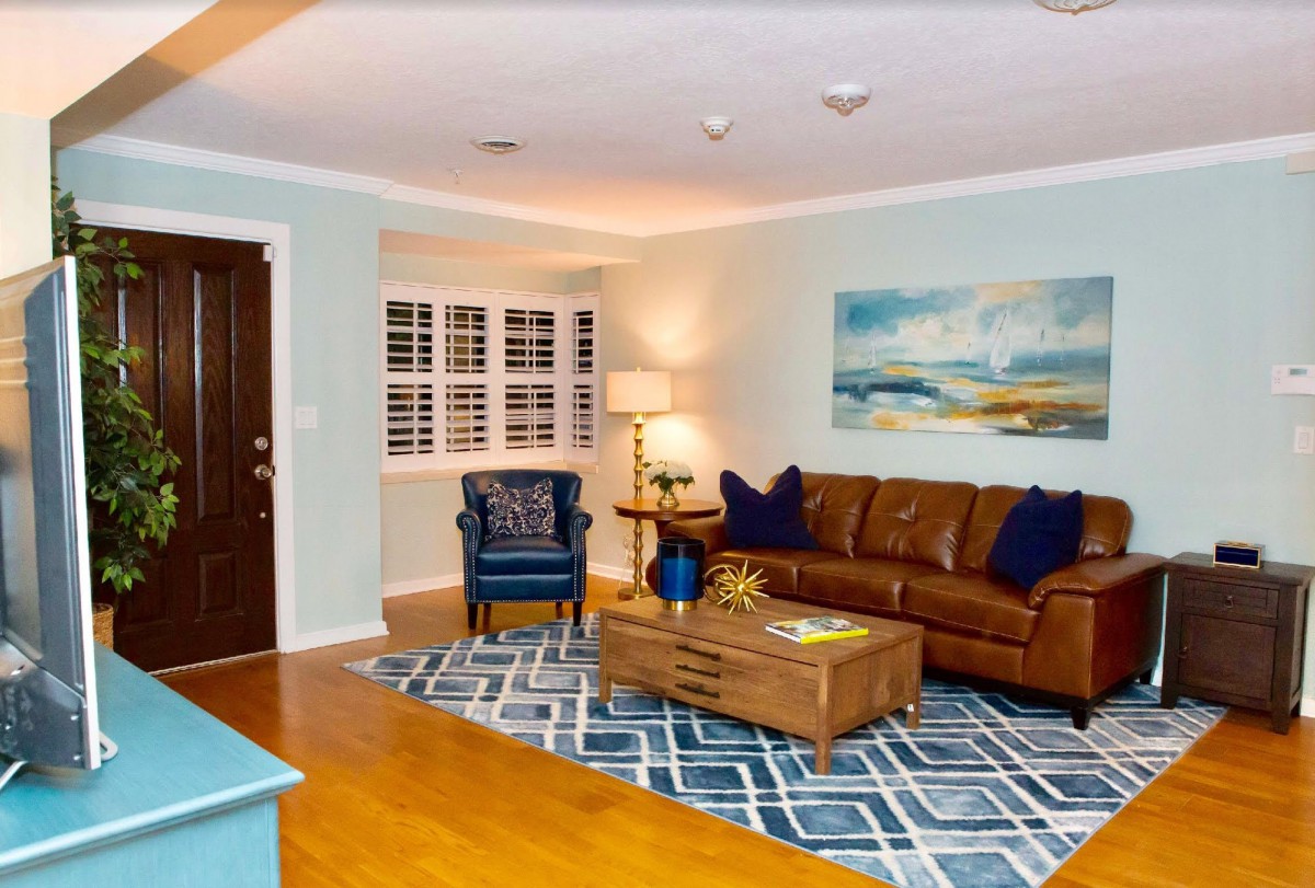 A cozy living room with a brown leather sofa, blue armchair, and decorative rug, featuring artwork on the wall.