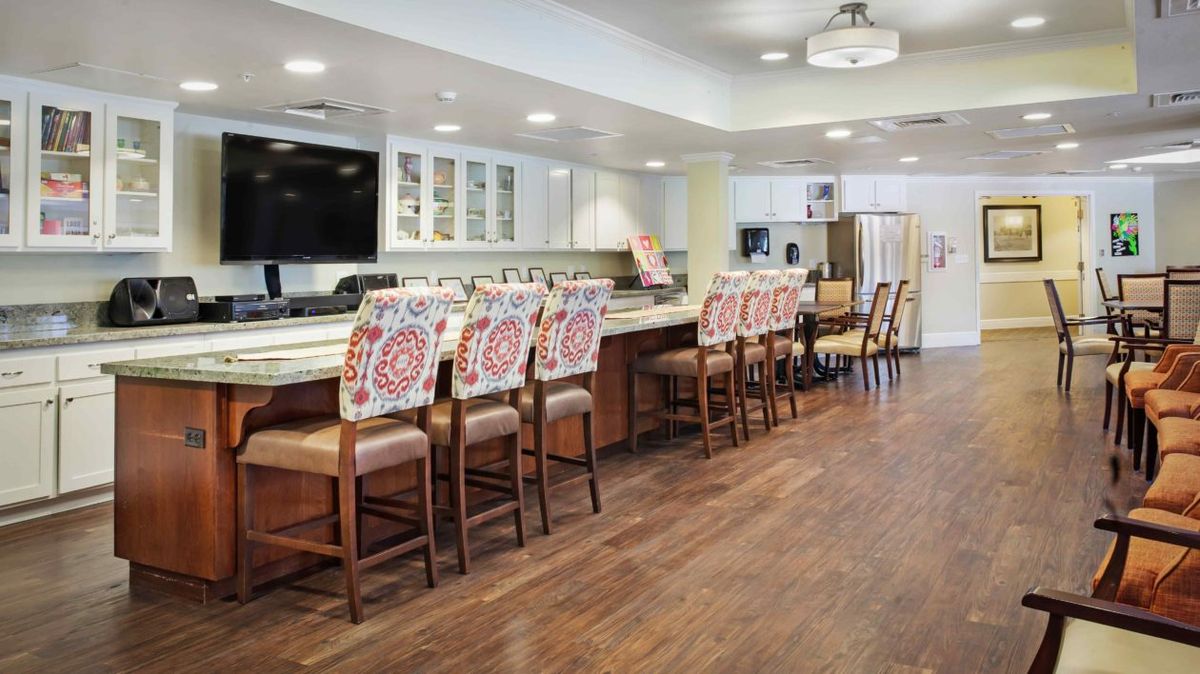 A modern kitchen with a large counter and colorful chairs, featuring wood flooring and contemporary lighting.