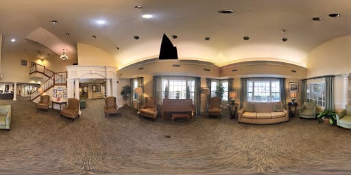A spacious lobby area with seating and a piano, featuring large windows and carpeted flooring.