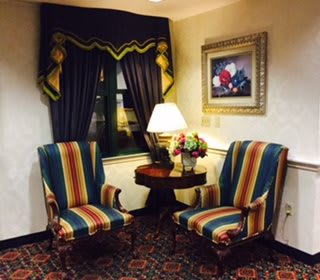 A cozy living room corner with striped chairs, a lamp on a table, and elegant curtains.