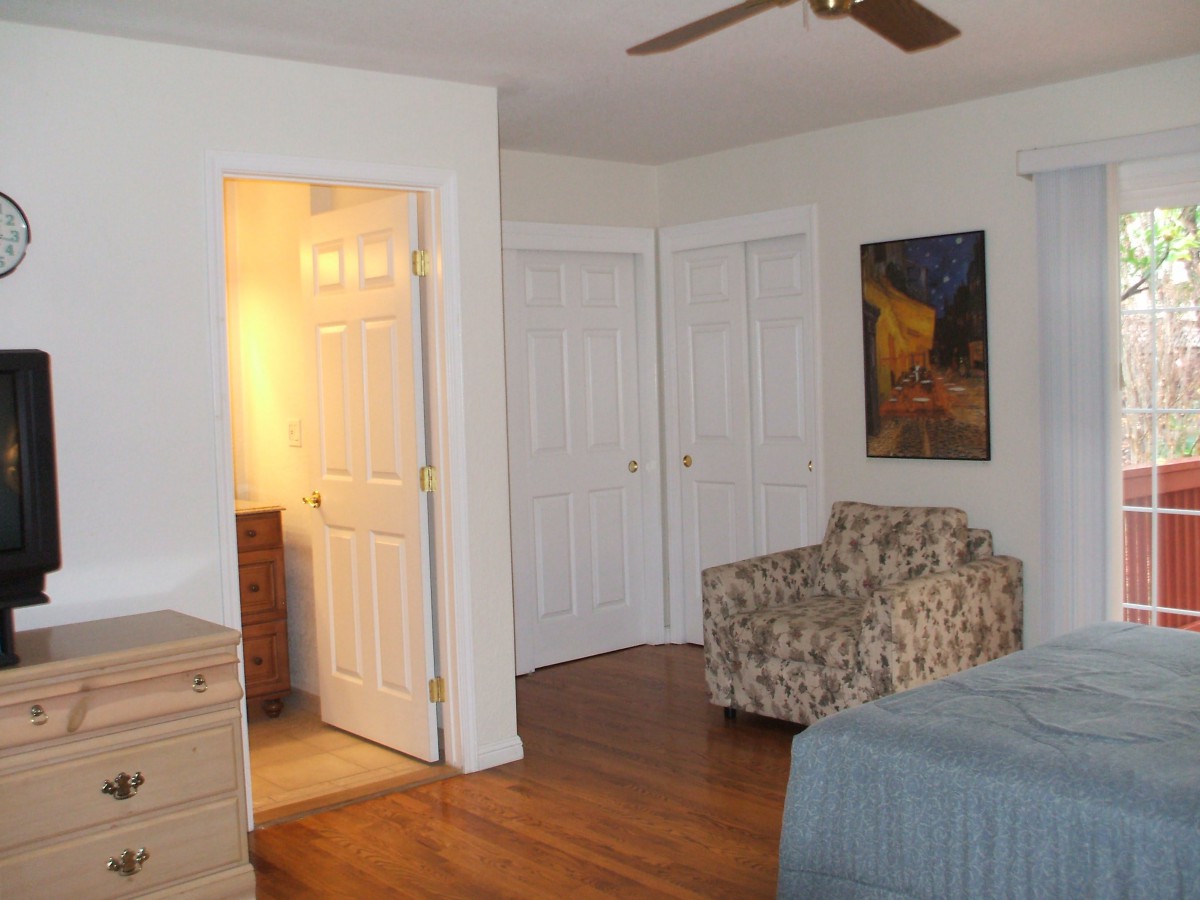 A cozy bedroom with a bed, patterned chair, closet doors, and a piece of artwork on the wall.