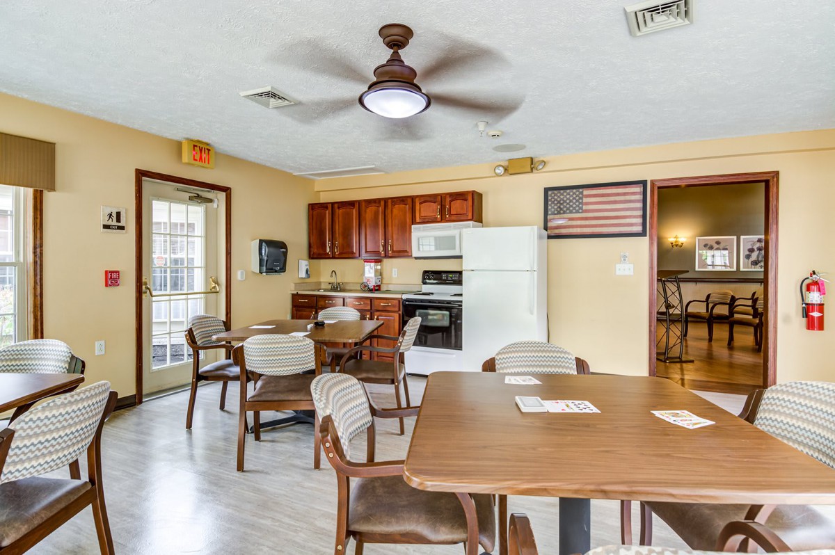 A kitchen and dining area with tables, chairs, a ceiling fan, and standard appliances like a fridge and oven.