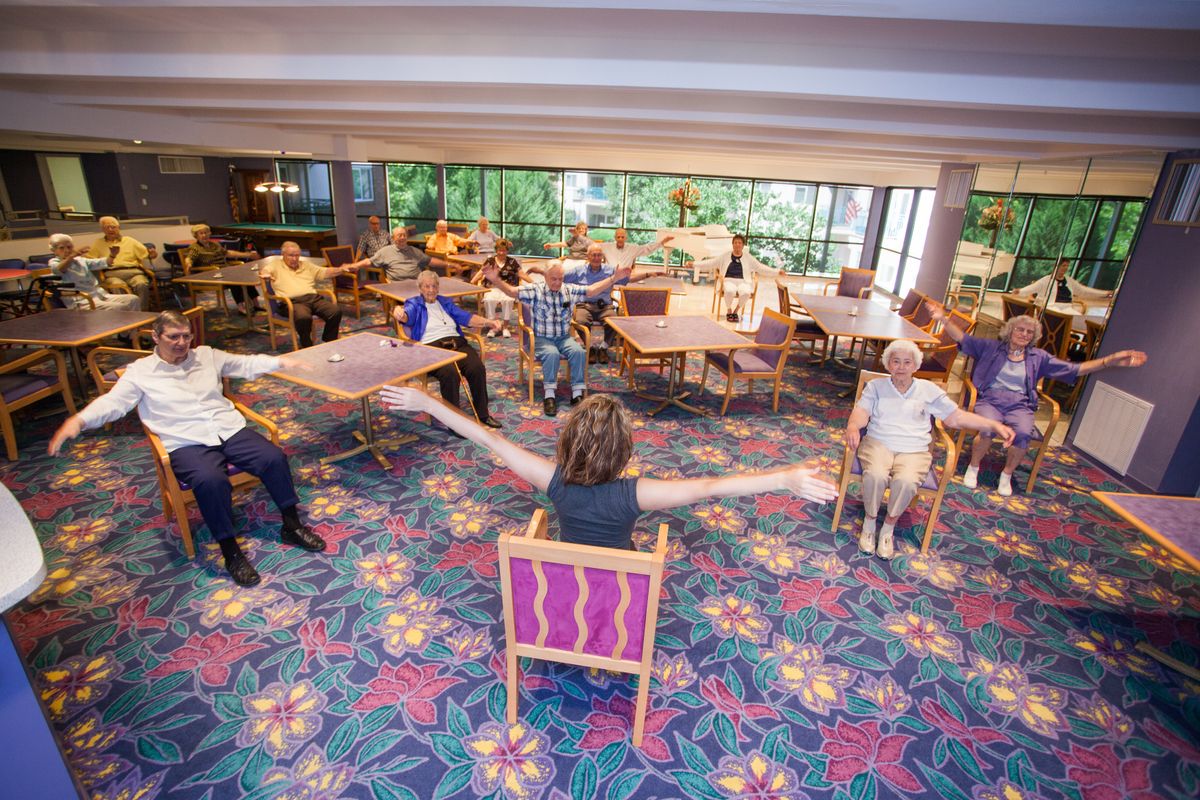 A group of senior citizens participating in a seated exercise class at a community center.