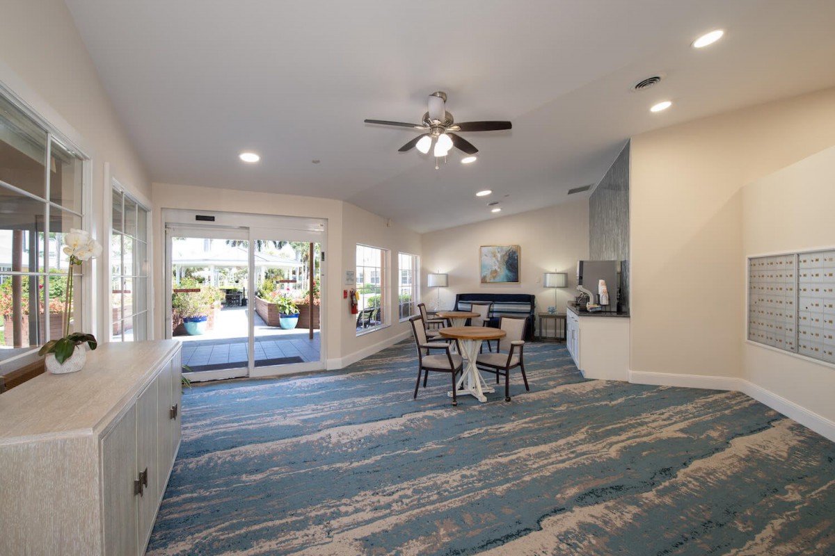 A modern living room with a patterned carpet, a ceiling fan, and sliding glass doors leading to the outside.