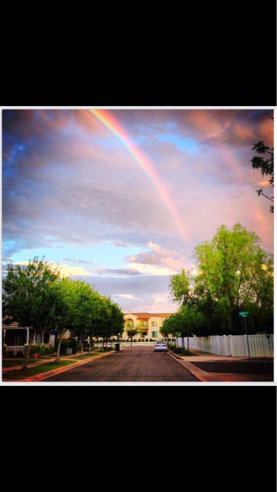 A beautiful rainbow arches over a peaceful neighborhood street at sunset.