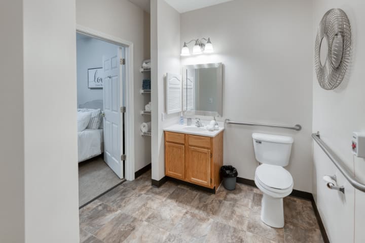 A modern bathroom with a wooden cabinet, large mirror, and sleek lighting fixtures.