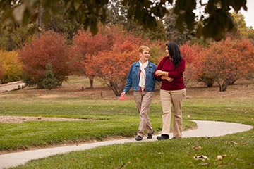 Two people walking arm in arm along a pathway in a park with autumn foliage.