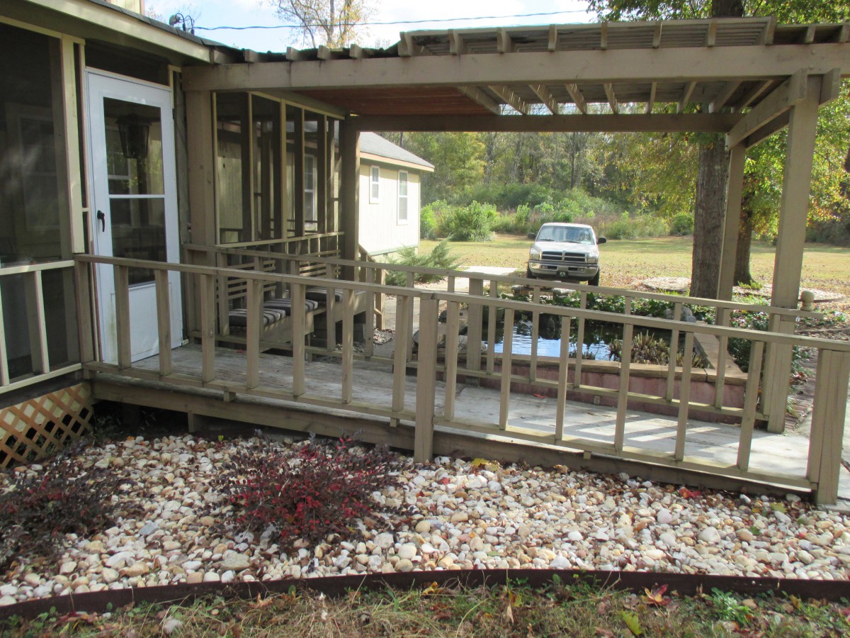 A wooden ramp leading from a house to a garden area with a parked car in the background.