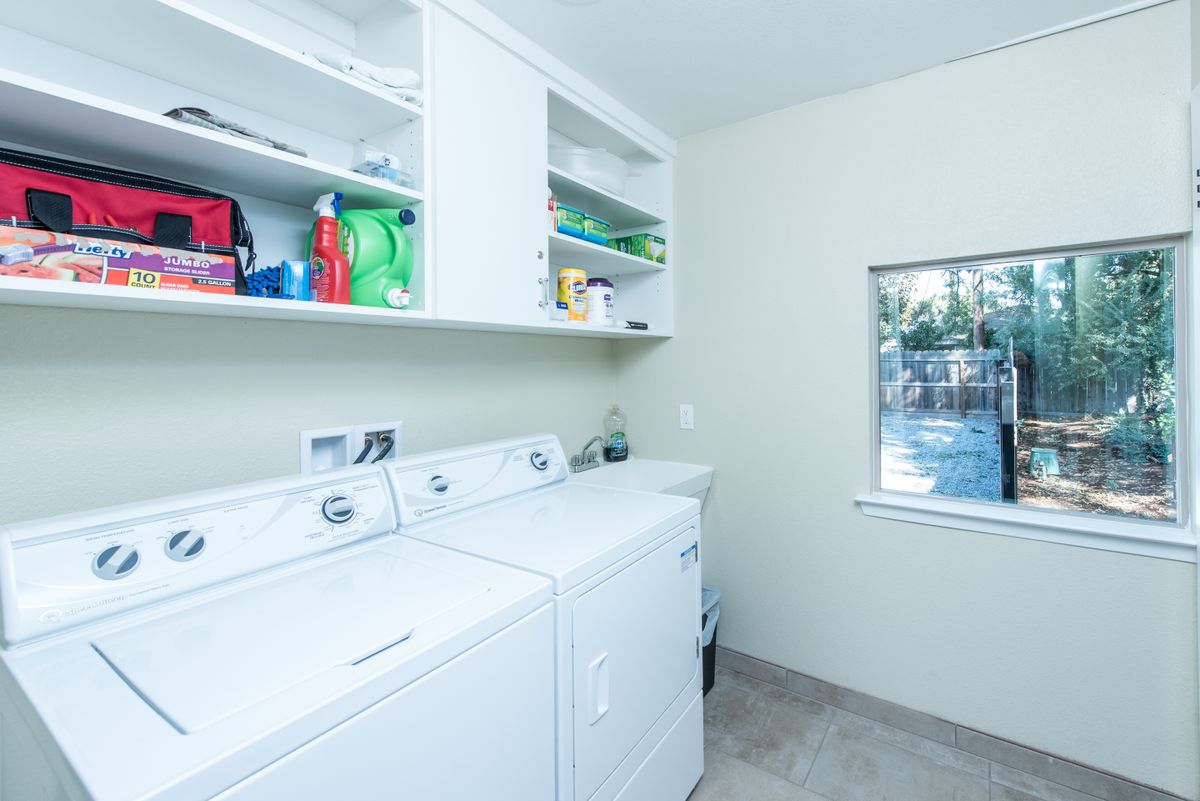 A bright laundry room featuring a washing machine, dryer, and shelves stocked with detergent.