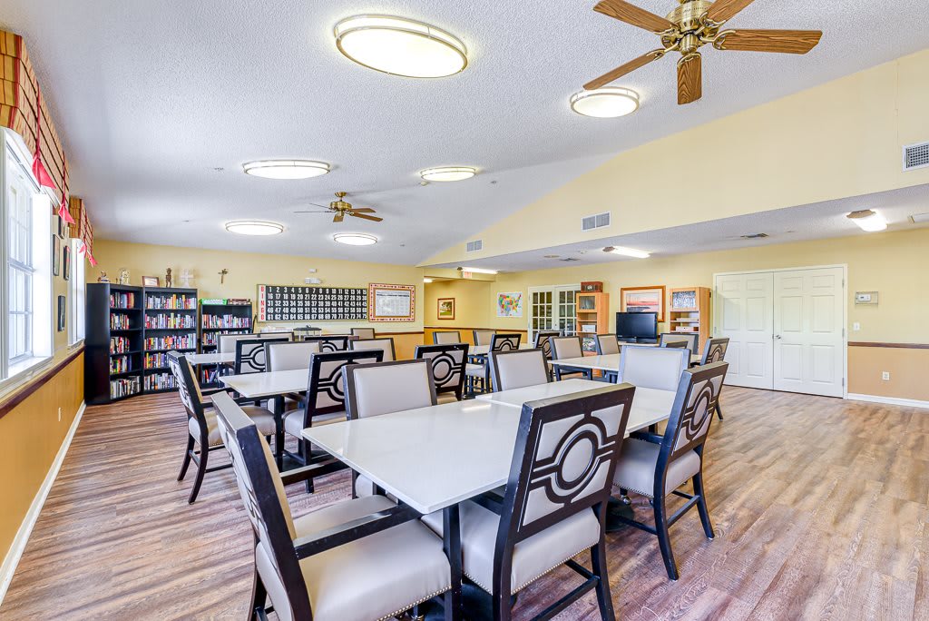 A spacious, well-lit dining area with multiple tables and chairs, featuring ceiling fans and library shelves.