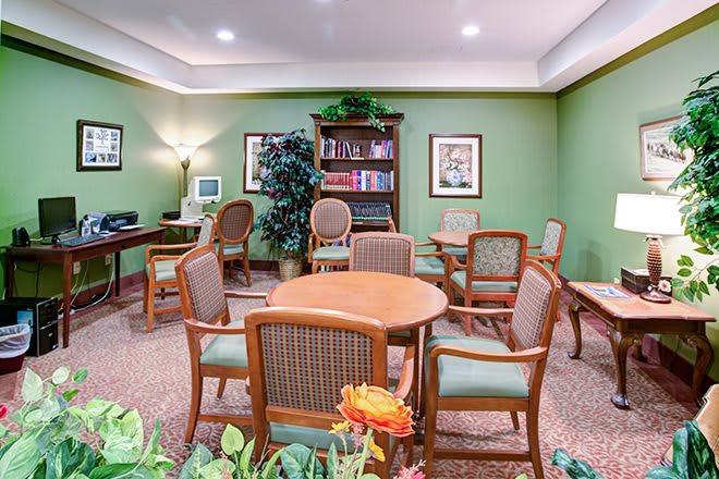 A cozy seating area with a round table, chairs, bookshelves, and decorative plants in a library setting.