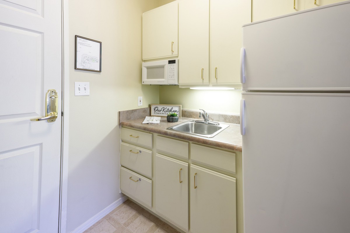 A compact kitchen featuring a microwave, fridge, and sink with beige cabinets and countertops.