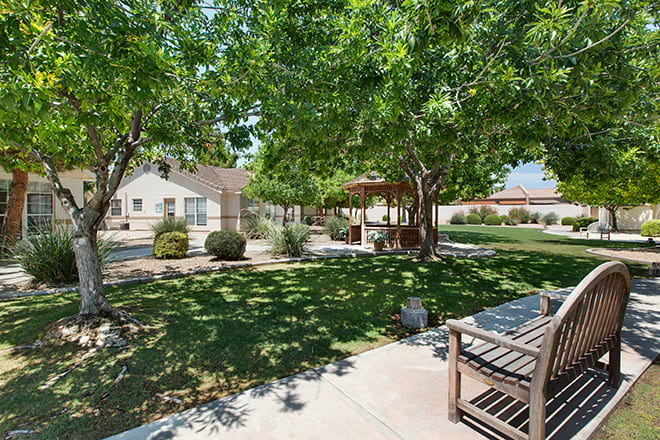 A peaceful garden with trees, a bench, and a gazebo on a sunny day.