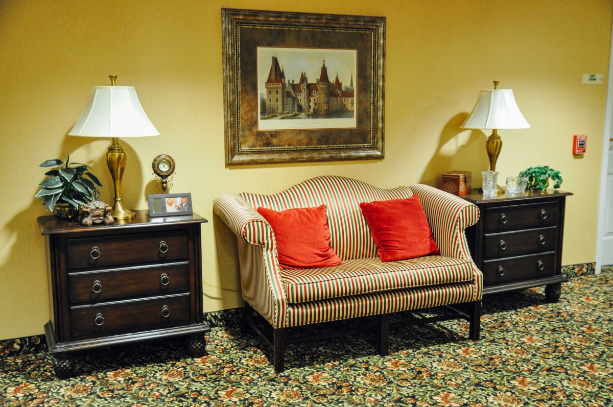 A vintage styled living area featuring a striped sofa with red cushions, flanked by two dark wooden side tables and lamps, set against a backdrop of warm yellow walls adorned with artwork.