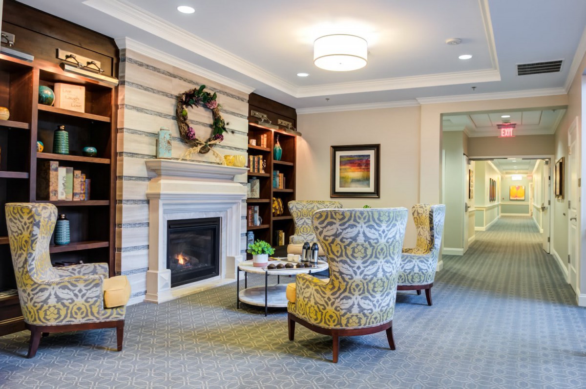 A cozy living room with a fireplace, decorated armchairs, and shelves filled with books and decor.