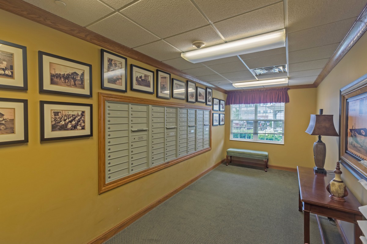 A hallway with framed photos and mailboxes on the wall, illuminated by overhead lighting.
