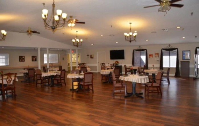 A spacious dining area with wooden floors, elegantly set tables, and chandeliers hanging from the ceiling.