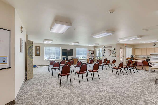 A spacious conference room with arranged chairs and tables, featuring a television and large windows.