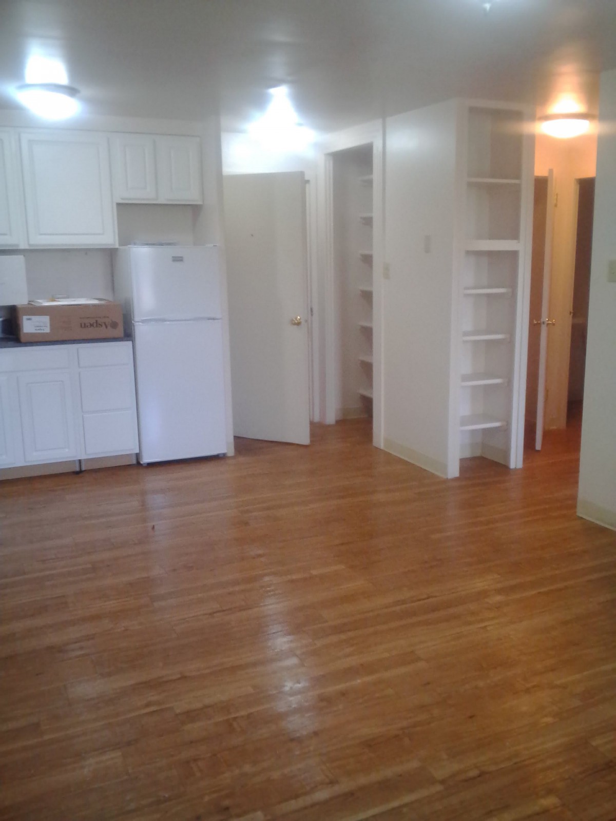 A minimalist apartment kitchen with wooden floors and white cabinetry.