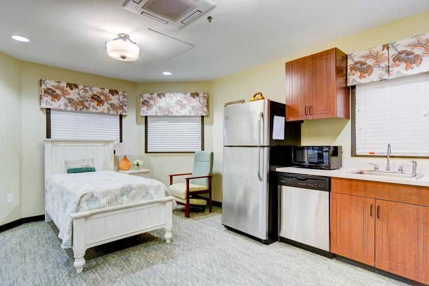 A cozy room featuring a bed, kitchenette, and modern appliances.