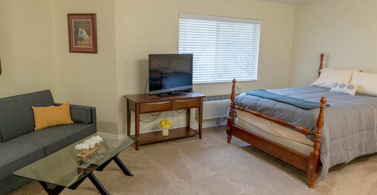 A cozy bedroom with a television on a wooden table and a bed next to a window.