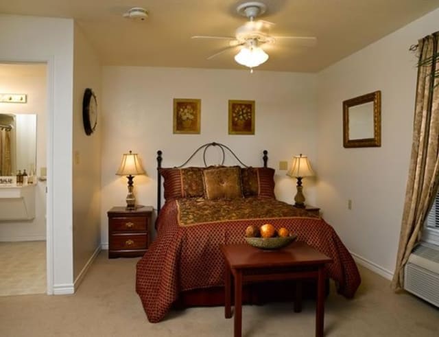 A cozy bedroom with a neatly made bed, side lamps, and decorative paintings.