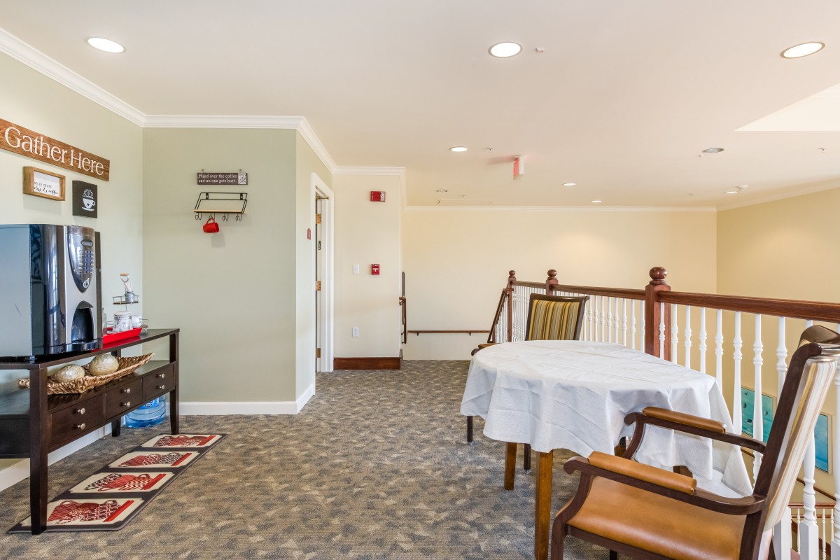 A cozy interior space with a dining area featuring tables and chairs, carpet flooring, and a railing.