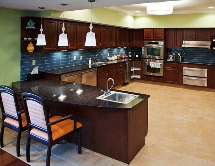 A modern kitchen featuring dark cabinets, a granite island with seating, and stainless steel appliances.