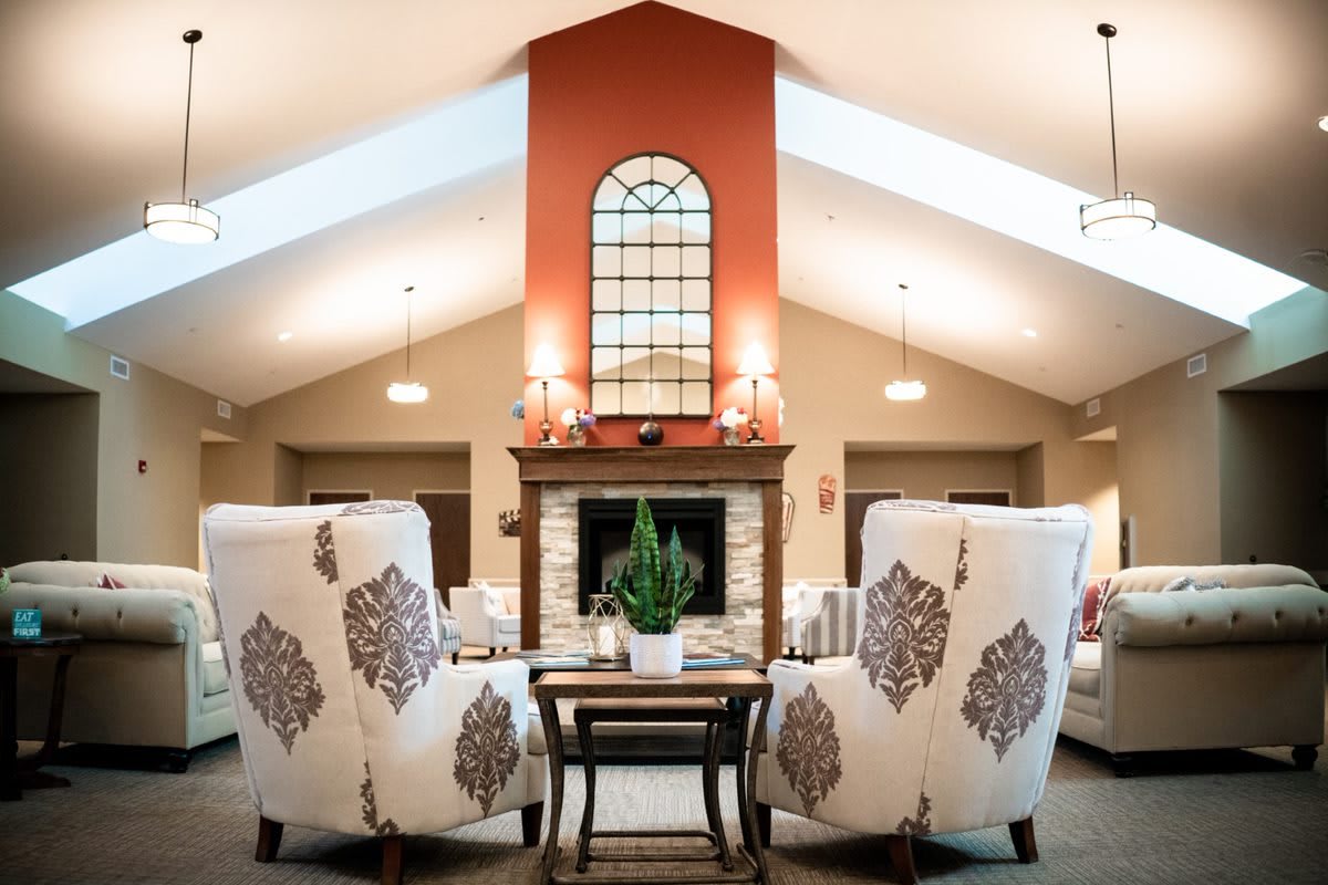 A cozy living room with elegant armchairs facing a brick fireplace, complemented by modern decor and a large window above.