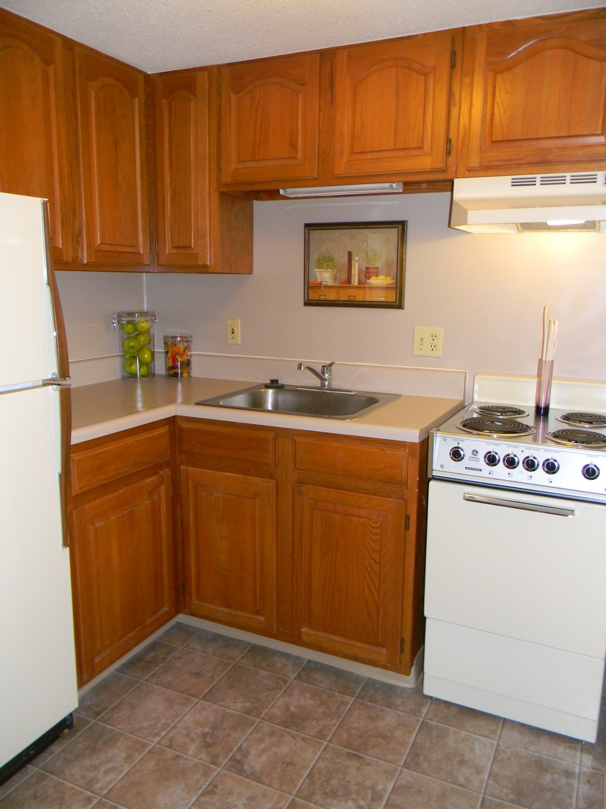 A small kitchen with wood cabinets, a refrigerator, stove, and sink.
