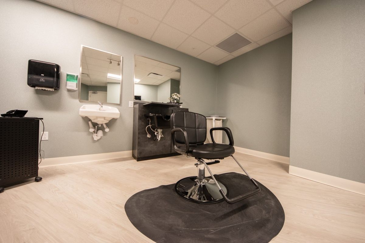 An empty modern hair salon with a barber chair, mirrors, and a sink.