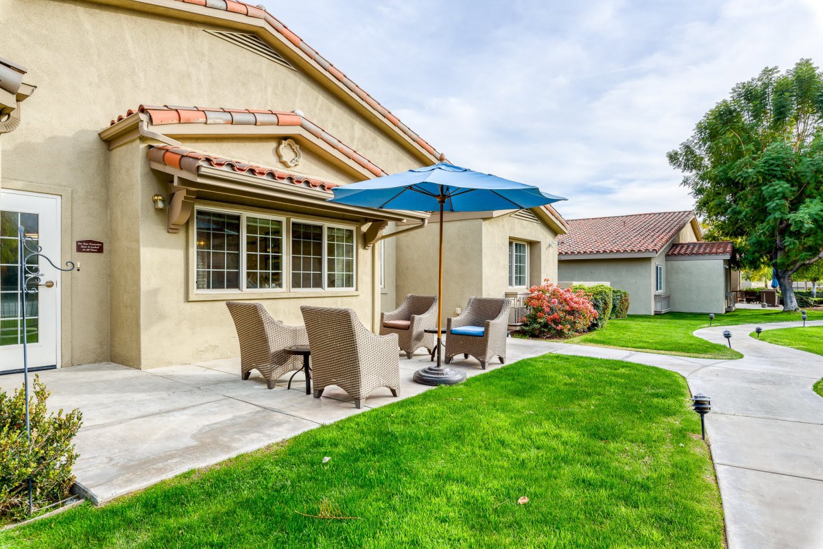 A cozy backyard patio with outdoor furniture and a blue umbrella.