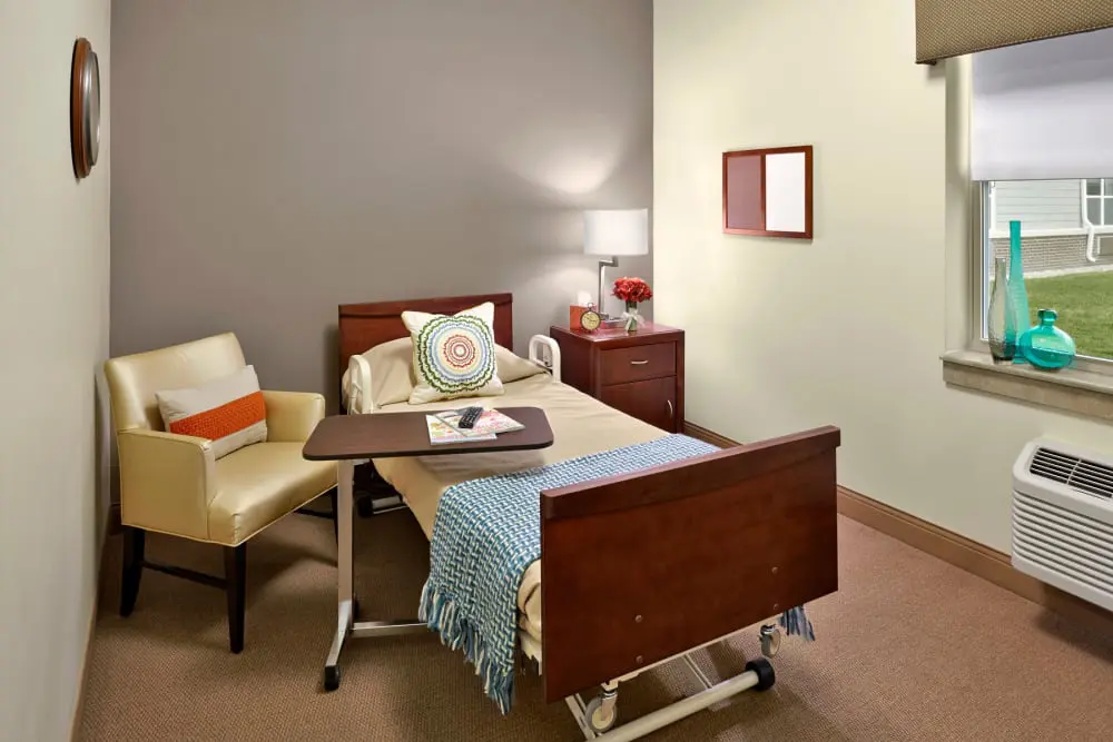 A hospital room with a bed, chair, and bedside table.