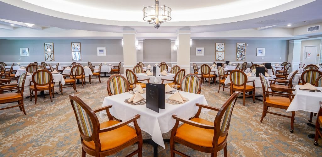 An elegant dining area with neatly arranged tables and chairs, featuring a central chandelier.