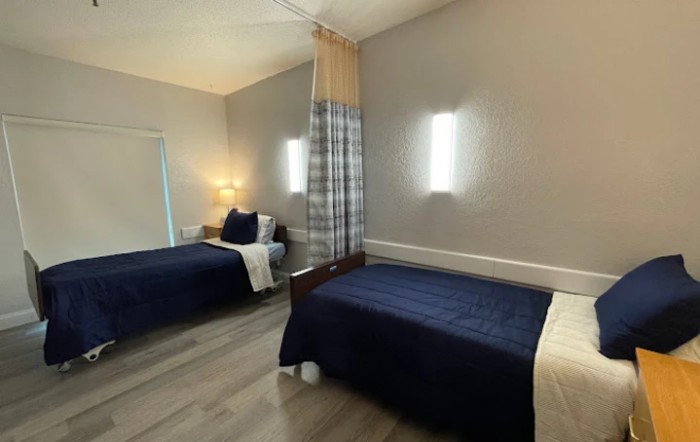 A modern bedroom with two beds, separated by a curtain, featuring sleek lighting and contemporary decor.