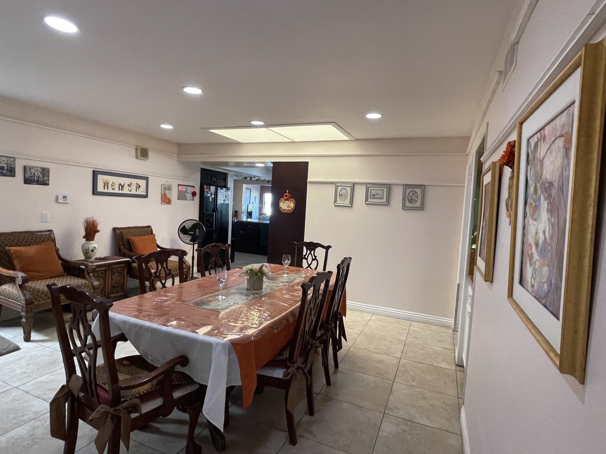 A spacious dining room featuring a large table with chairs, adorned with artwork on the walls and well-lit by ceiling lights.
