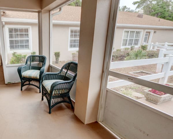 A cozy screened porch with two wicker chairs, overlooking the outside view.